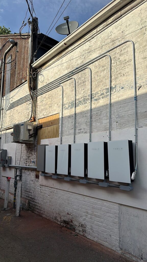 Five Tesla battery units with parallel conduit runs on the back wall